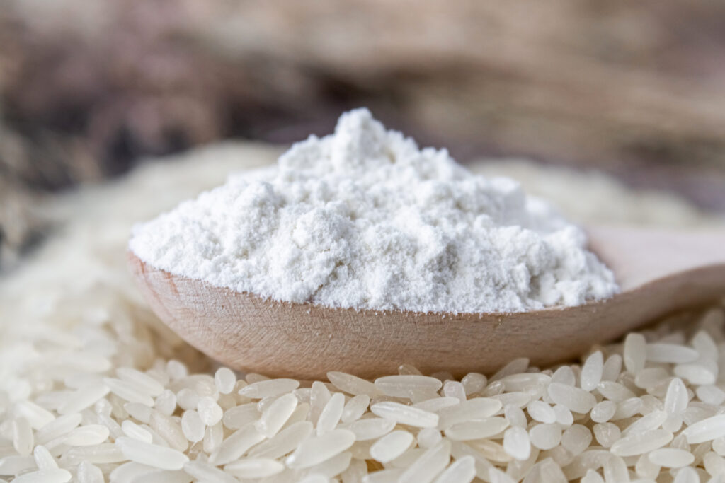 rice flour in a spoon on a pile of white rice on old boards.