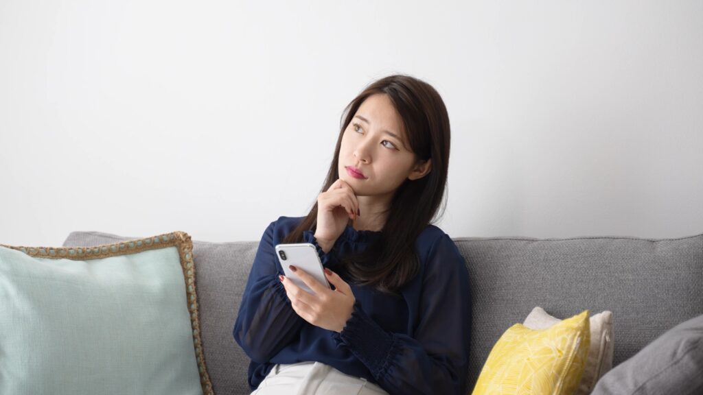 スマートフォンを持って考え事をする女性